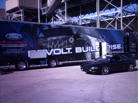 1995 Ford Probe - A black coupe sits in front of a large trailer graphics and branding for Ford Racing and Cosworth.