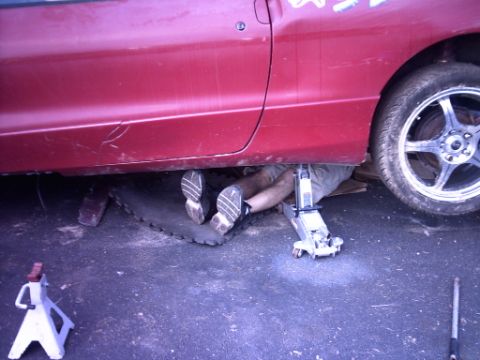 1995 Ford Probe - A person works on the underside of a red 1995 Ford Probe, which is raised on a jack and jack stands.