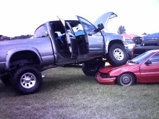 Silver lifted pickup truck with doors open, hood up, crushing a red car's front end