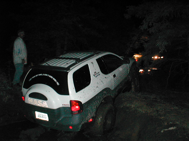 White Isuzu VehiCROSS with NASA spare tire cover and JEEBUS plate on a rocky trail at night