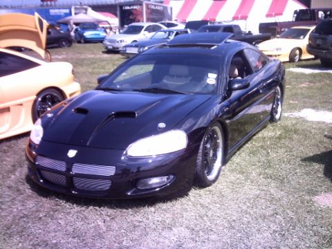 1995 Ford Probe - A black coupe with aftermarket wheels and hood scoops is displayed at an outdoor car show.