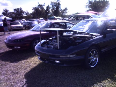 1995 Ford Probe - Two sports cars, a black 1995 Ford Probe and a red car, are parked side-by-side at a car show.