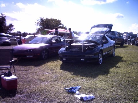 1995 Ford Probe - Two cars are parked on the grass at an outdoor event, one with its hood open.