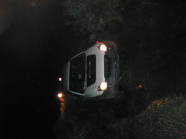 White SUV with headlights on at night on a dark wooded trail