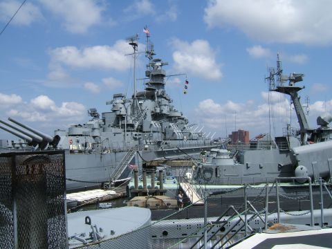 1998 Ford Taurus - A large battleship is docked next to a submarine, with a clear blue sky and scattered clouds overhead.