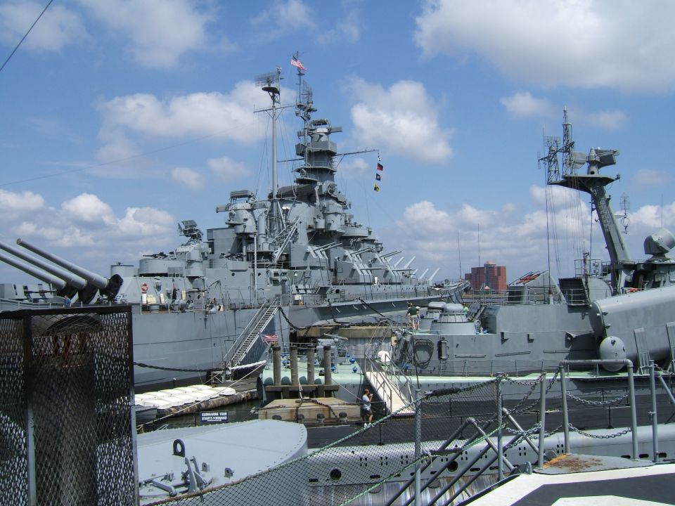 battleship with large guns docked next to a submarine under a cloudy sky