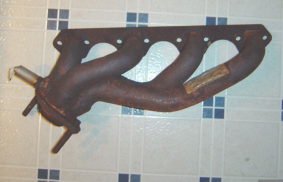 Rusty four-port tubular cast iron exhaust manifold with O2 sensor bung on tile floor