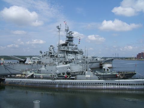 1998 Ford Taurus - A large battleship is moored alongside a submarine in a harbor under a partly cloudy sky.