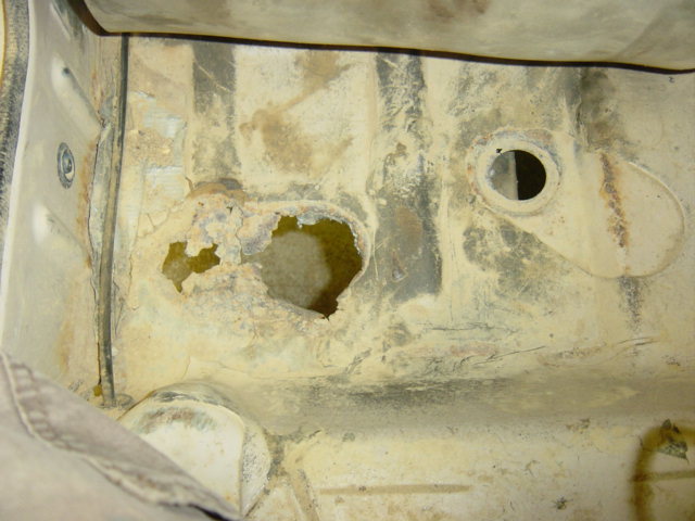rusted out section of a vehicle's undercarriage, showing holes and corrosion