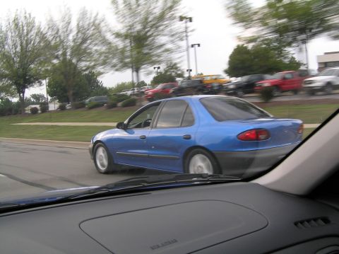 1996 Chevrolet Cavalier - A blue 1996 Chevrolet Cavalier sedan drives by, captured from another vehicle.