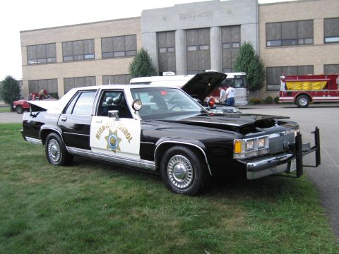 1991 Ford Crown Victoria - This police car has a push bumper and a light bar on the roof. The hood is open, revealing the engine compartment.