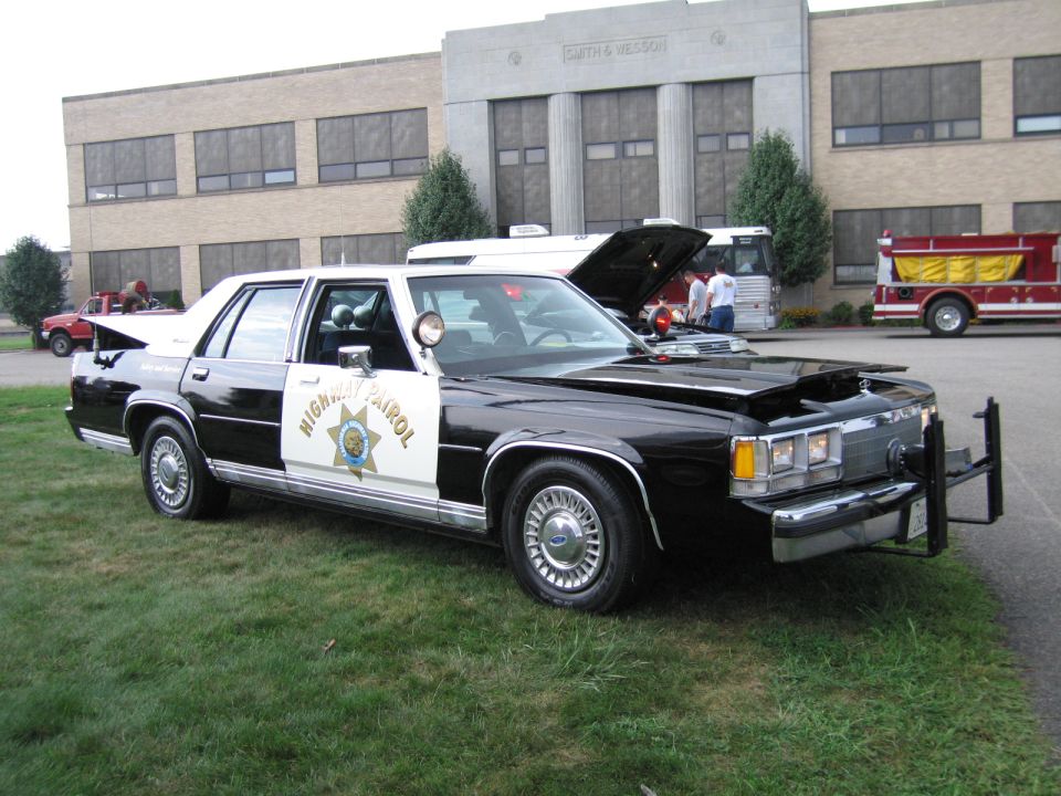 CHP black and white Ford sedan with raised hood at an outdoor show