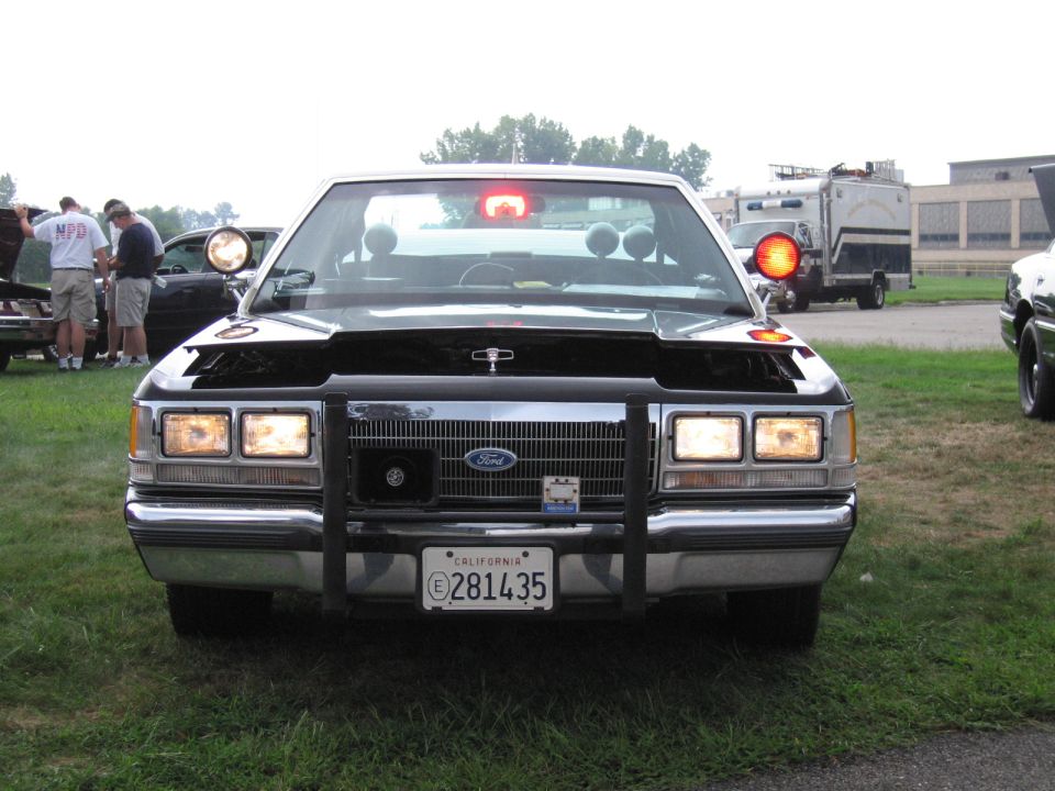 Front view of a black Ford sedan with push bar and California plate 281435