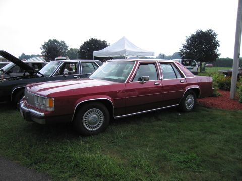 1991 Ford Crown Victoria - Two sedans are parked on a grassy area with a white tent visible behind them.