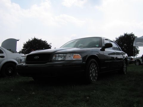 1991 Ford Crown Victoria - A black Ford Crown Victoria is seen from the front-right at an outdoor event, with another vehicle's hood open nearby.