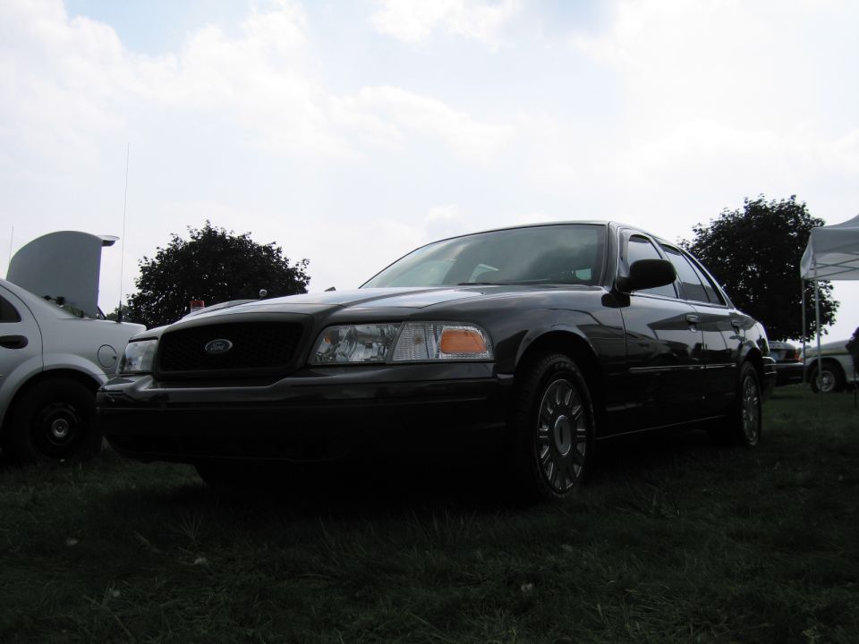 Dark Ford Crown Victoria sedan front quarter view on grass under cloudy sky