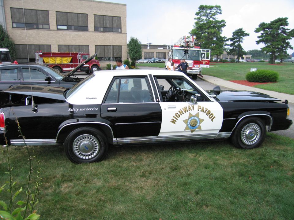 Black-and-white Highway Patrol sedan with star door shield parked outside a building