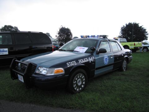 1991 Ford LTD Crown Victoria - blue-and-gray State Police 947 Ford Crown Victoria with push bar and roof light bar parked on grass.