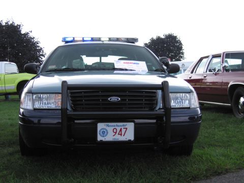 1991 Ford LTD Crown Victoria - Head-on view of a dark police Ford Crown Victoria with push bar and Massachusetts '947' plate under a blue light bar.