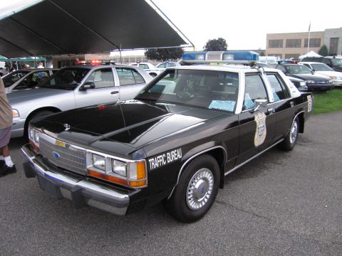 1991 Ford LTD Crown Victoria - black Ford LTD Crown Victoria Traffic Bureau police car with door shield and light bar parked under a show tent.