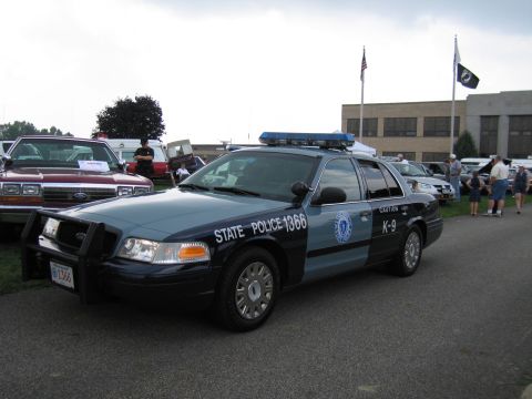 1991 Ford LTD Crown Victoria - blue-and-gray Ford Crown Victoria marked State Police 1366 K-9 with push bar, flags flying in the background.