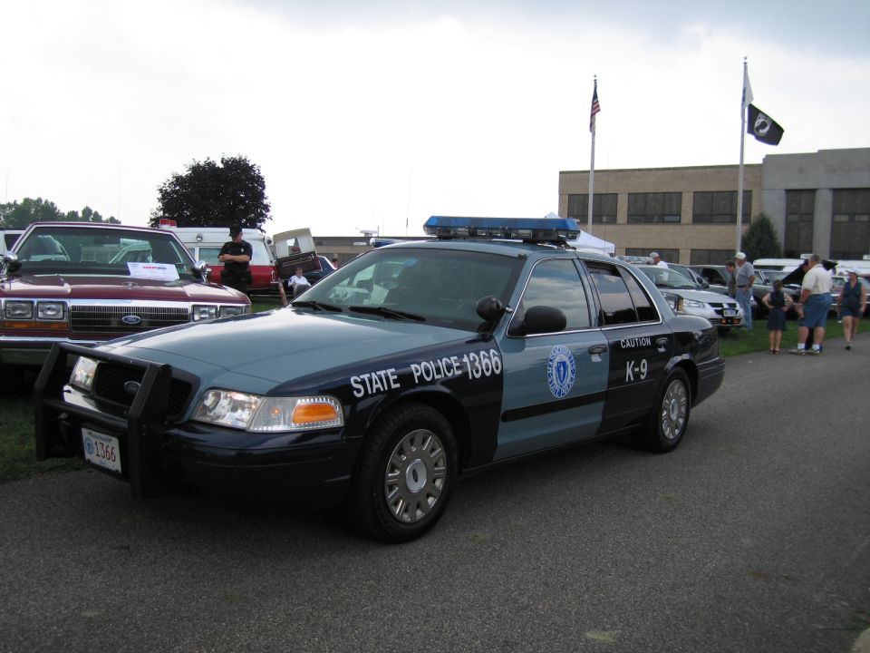 Blue-gray State Police 1366 K-9 Ford Crown Victoria cruiser with flags behind