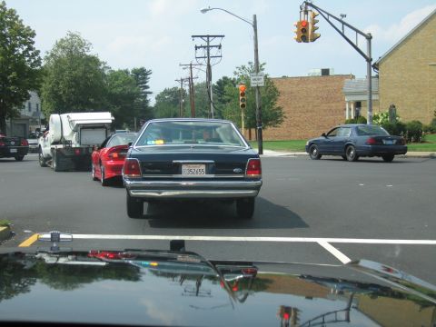 1991 Ford LTD Crown Victoria - View through a windshield of a dark full-size sedan at an intersection, a red car and traffic signal nearby.