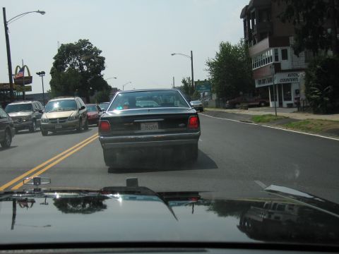 1991 Ford LTD Crown Victoria - Windshield view of a dark sedan with plate 352655 ahead on a city street near a McDonald's sign.