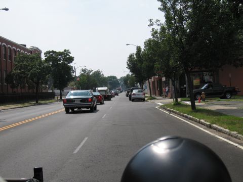 1991 Ford LTD Crown Victoria - dark sedan turns on a tree-lined urban street, photographed over a black spherical foreground object.