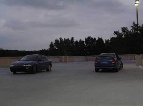 1996 Chevrolet Cavalier - Two blue sedans are parked on a rooftop with trees in the background and a street light overhead.