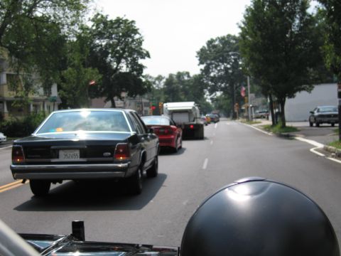 1991 Ford LTD Crown Victoria - dark Ford sedan with plate 352655 sits in traffic behind a red car and a box truck on a tree-lined road.