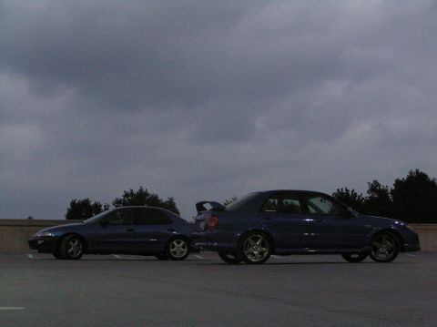 1996 Chevrolet Cavalier - Two blue sedans are parked next to each other on a paved surface with trees in the background.
