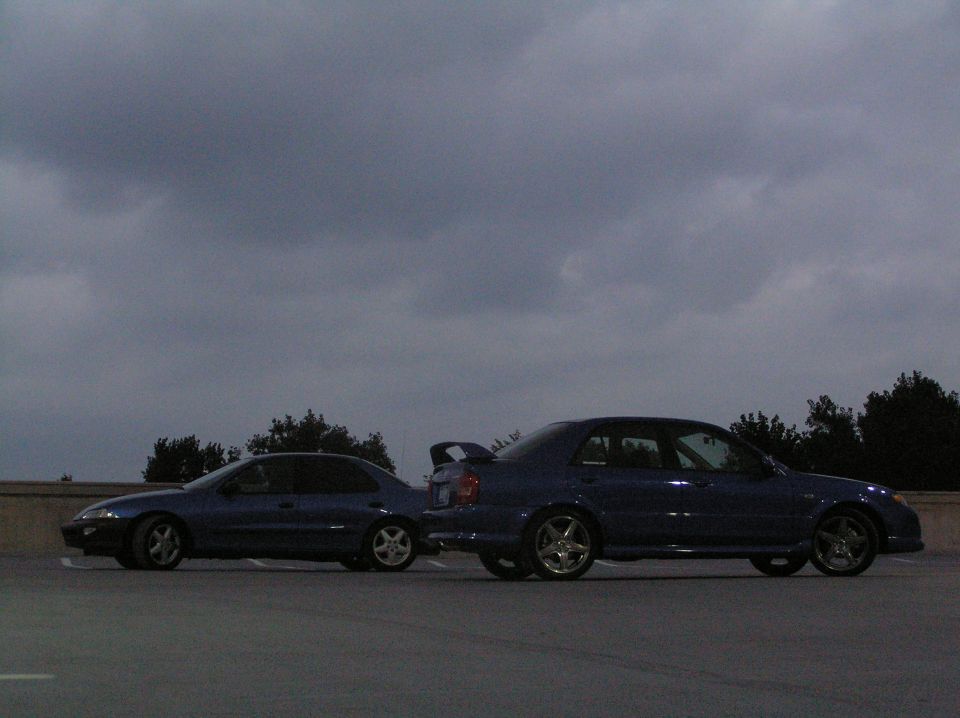 two blue sedans parked side by side under a cloudy sky