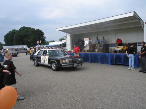 1991 Ford LTD Crown Victoria - black-and-white Highway Patrol Ford sedan parked on pavement near a covered stage and crowd at an event.