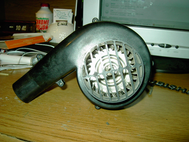 Black plastic blower fan housing with metal impeller on a wooden desk