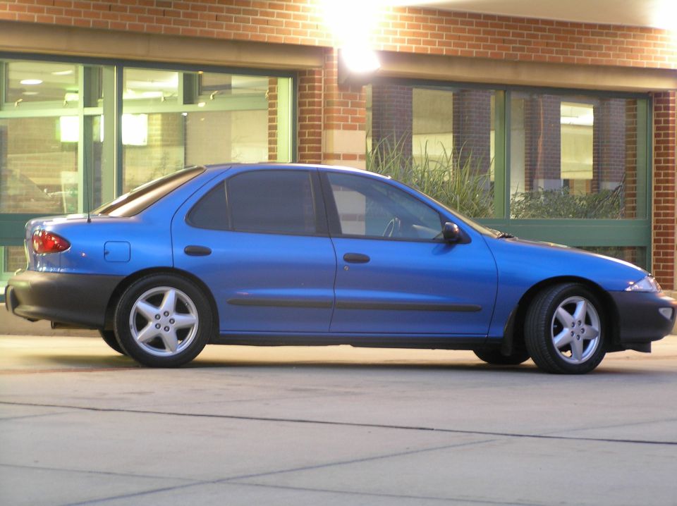Blue Chevrolet Cavalier four-door sedan in side profile outside a brick building
