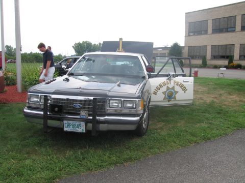 1991 Ford LTD Crown Victoria - silver-and-black Ford police sedan badged Highway Patrol with a front push bar and open door, plate CHP8849, on a lawn.