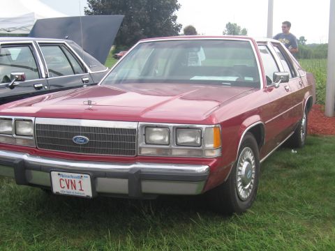 1991 Ford LTD Crown Victoria - red Ford full-size sedan with a Massachusetts vanity plate reading CVN 1 parked on grass at a show.