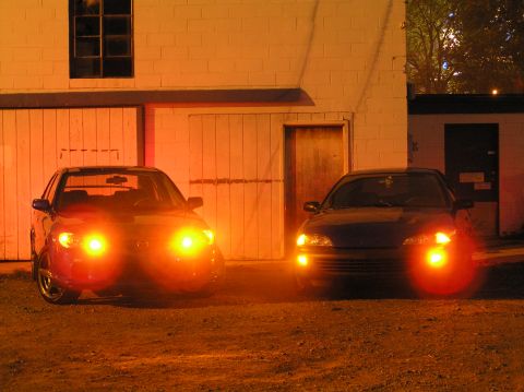 1996 Chevrolet Cavalier - Two cars are parked outside a building at night with their headlights illuminated.