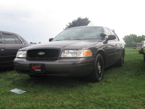 1991 Ford LTD Crown Victoria - gray Ford full-size sedan with steel wheels and a red DARE placard mounted on the grille, parked on grass.