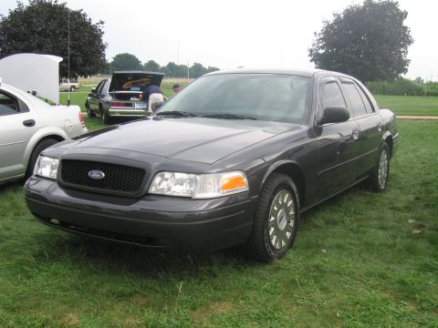 1991 Ford LTD Crown Victoria - dark gray Ford full-size sedan with painted steel wheels parked on grass at an outdoor gathering.