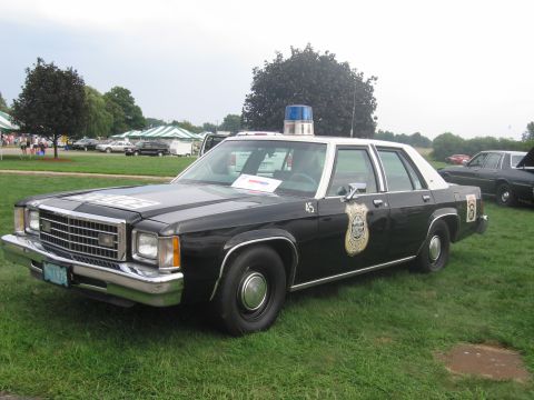 1991 Ford LTD Crown Victoria - black-and-white Ford full-size police sedan with a blue roof beacon and door shield marked 45 on grass.