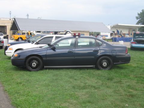 1991 Ford LTD Crown Victoria - Side profile of a dark blue Chevrolet Impala police sedan with steel wheels and a roof light bar on grass.