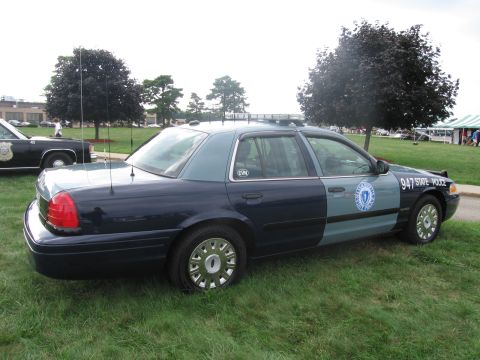 1991 Ford LTD Crown Victoria - Rear three-quarter view of a blue-and-gray Ford State Police cruiser marked 947 with whip antennas on grass.