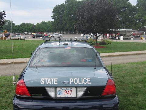1991 Ford LTD Crown Victoria - Rear of a dark green-blue Ford lettered STATE POLICE with twin whip antennas and Massachusetts plate 947 on grass.