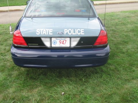 1991 Ford LTD Crown Victoria - Close rear view of a blue-green Ford sedan lettered STATE POLICE with a Massachusetts 947 plate parked on grass.