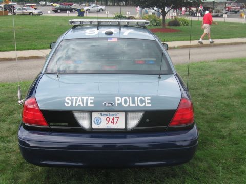 1991 Ford LTD Crown Victoria - Rear view of a blue-gray Ford State Police cruiser marked 947 with whip antennas, a person walking in the background.