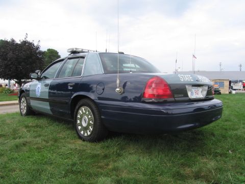 1991 Ford LTD Crown Victoria - Rear three-quarter view of a blue-and-gray Ford State Police cruiser with whip antennas parked on grass near flags.