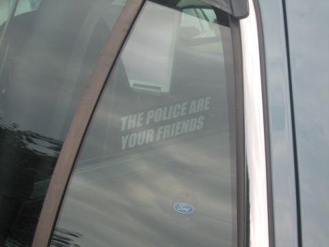 1991 Ford LTD Crown Victoria - rear-door window of a dark car bears a decal reading THE POLICE ARE YOUR FRIENDS above a Ford oval emblem.