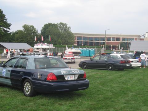 1991 Ford LTD Crown Victoria - dark teal State Police sedan with a Massachusetts plate sits on grass, with more parked cars and a large building in the background.